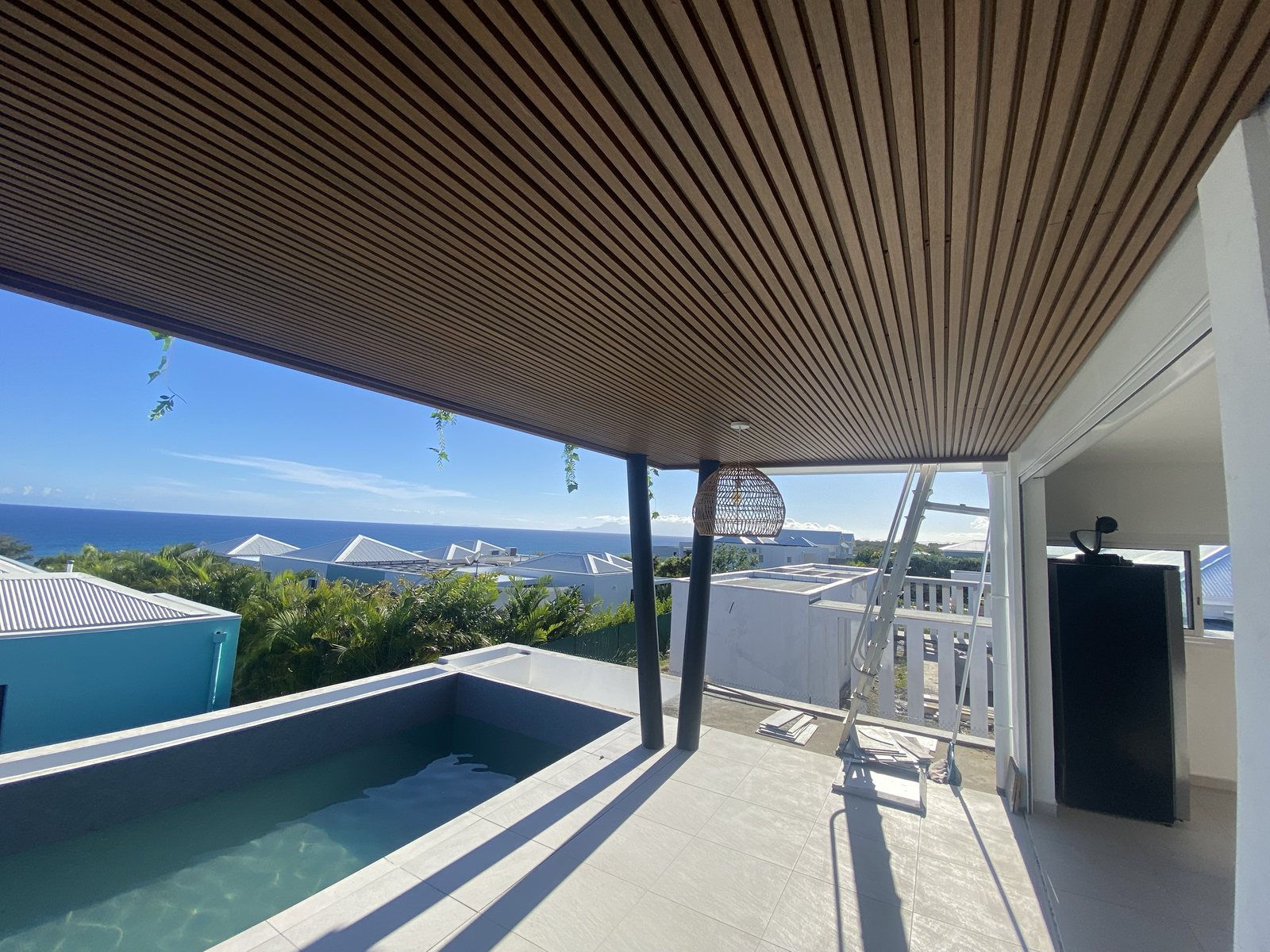 Plafond en lames composites au-dessus d'une terrasse avec piscine face à la mer